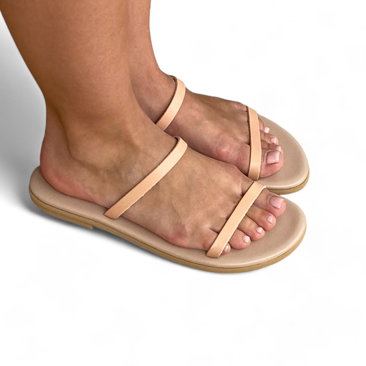 Close-up of feet wearing beige flat sandals with two thin straps, on a light background.